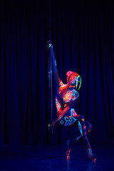 Female pole dancer in bright neon colours under ultraviolet (UV) light on background