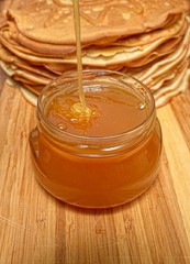 Honey flows from above in a glass jar against pancakes