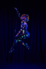 Naklejka na ściany i meble Female pole dancer in bright neon colours under ultraviolet (UV) light on background