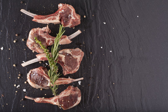 fresh lamb, fillet of red fresh rack of lamb cut in 5 pieces seasoning salt pepper and rosemary on black stone background