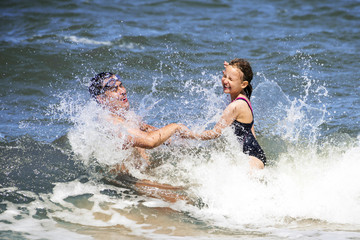 Happy child girl with father playing in the waves.