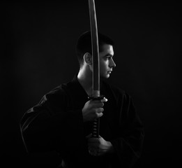 Young martial arts fighter with katana on black background, black and white.