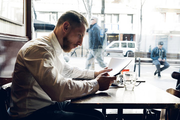 Portrait of a confident man entrepreneur studying important paper documents before business meeting while sitting in modern coffee shop interior in urban setting