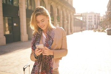 beautiful young woman with blonde hair messaging talking on the smart-phone at the city street background. pretty girl talking on the phone in the glow the setting sun