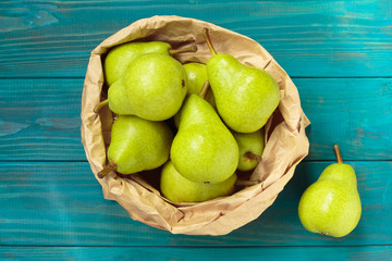 green pears in paper bag on blue wooden background, top view.
