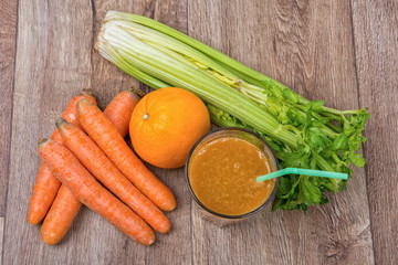 Blended orange smoothie with ingredients on wooden table