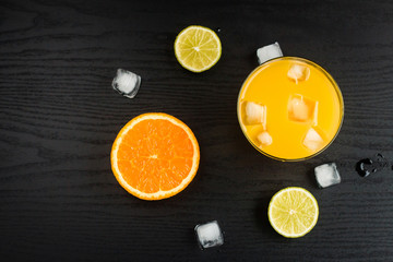 Fresh orange juice, orange and lime slices and ice on black background
