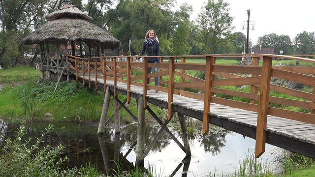Happy woman walk from wooden bower on bridge through sink river in park. Static shot.
