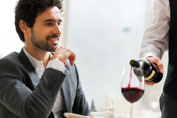 Waiter pouring red wine to a man
