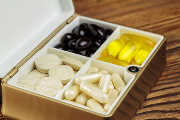 Mixed natural food supplement pills in container, omega 3, vitamin c, carotene capsules on wooden background