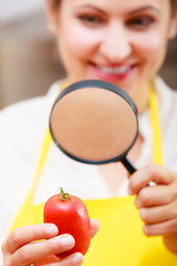 Woman inspecting tomato with magnifying glass.