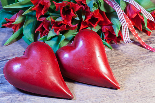 Zwei rote liegende Herzen vor einem Strauß Tulpen auf altem Holztisch