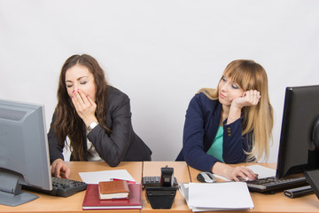 Two young office employee wearily sitting behind a desk