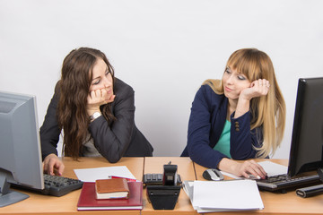 Two young office employee wearily looking at each other behind a desk