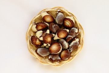 chocolate candy shaped sea shells in a wicker basket on the white tablecloth
