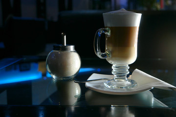 Glass of latte coffee shugar and spoon on glass table.