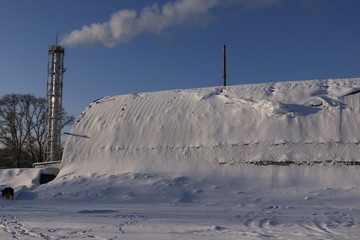 Fototapeta premium Труба с дымом и ангар, покрытый снегом, зимним солнечным днем