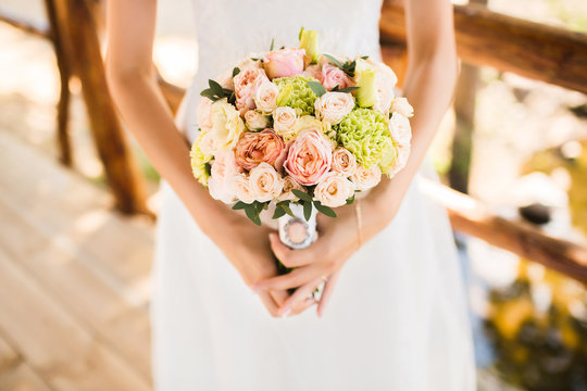 Only visible hand with  bouquet and white dress. Bouquet of roses.