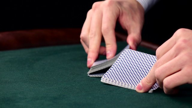Croupier shuffle cards, shows one on green table at casino