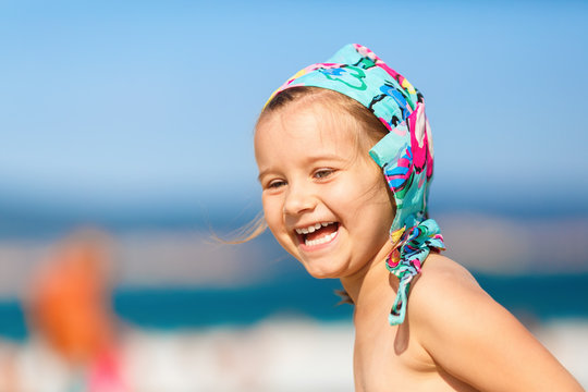 Close-up of baby girl with a bandanna on his head on a blurred background of blue sky and sea. Laughing happy child. Hot sunny summer day. Selective focus.