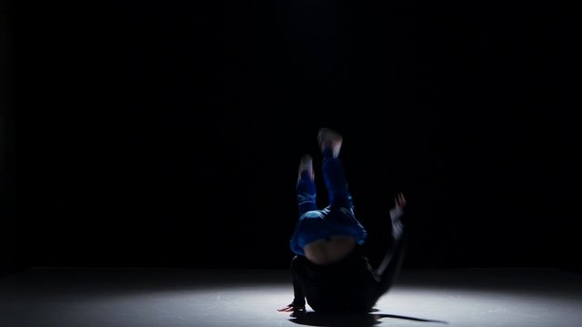 Boy in blue trousers dancing breakdance, on black, shadow