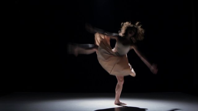 Young woman dancer dancing contemporary dance moves, jumps and makes a split, on black, shadow