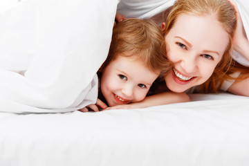 happy family mother and child playing and laughing in bed