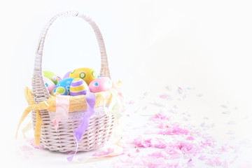 Fototapeta na wymiar Colorful Easter eggs in white basket and pink delicate blossoms
