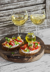 Tomato and cheese bruschetta and two glasses of white wine on a rustic wooden cutting board. Healthy breakfast, snack or appetizer with wine