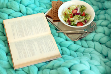Open book, plaid and coffee on sofa. Top view