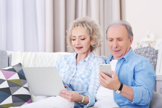 Mature couple using laptop and mobile phone at home