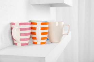 Set of striped cups on shelf against white wall background