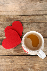 Cup of coffee with red felt hearts on wooden background, close up