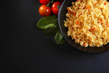 Stewed rice with a carrot and tomatoes on a plate over black background, close up