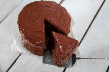 Chocolate cake with a cut piece on wooden table background, closeup