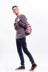 Fototapeta premium Happy hipster guy in glasses with backpack using a smart phone to listen music with headphones on white background