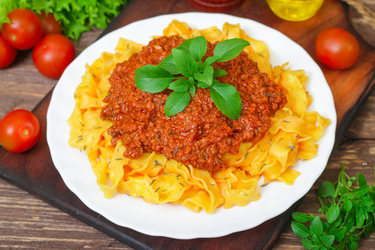 Traditional Italian pasta Bolognese or Bolognese with cooked pasta noodles topped with a spicy tomato based meat sauce garnished with fresh basil on a wooden background