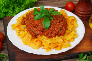 Traditional Italian pasta Bolognese or Bolognese with cooked pasta noodles topped with a spicy tomato based meat sauce garnished with fresh basil on a wooden background