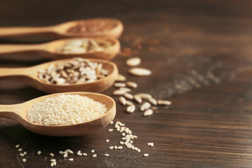 Sesame, flax, pumpkin and sunflower seeds in wooden spoons on table, closeup