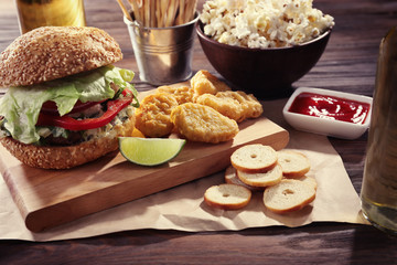 Big tasty hamburger with snacks and glass bottle of light beer on wooden table