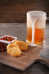 Glass mug of light beer with snacks on wooden table, close up