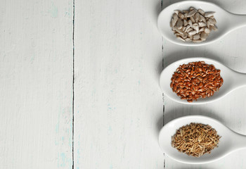 Different kinds of seeds in spoons on wooden table