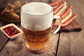 Glass of beer, chicken wings and grilled sausages on wooden table, close up