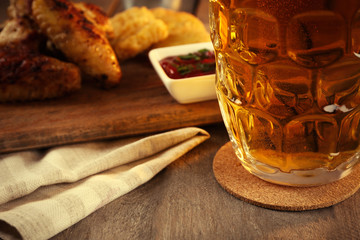 Glass of beer and chicken wings on wooden table, close up