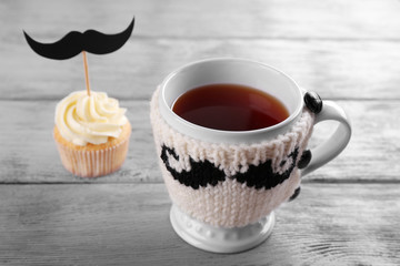 Delicious creative cupcake with mustache and cup of tea on wooden table