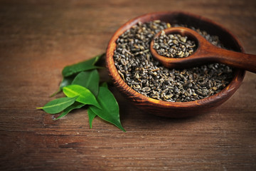 Granulated tea with green leaves in wooden bowl on table closeup