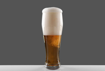 Glass of draft lager beer with thick froth on grey background