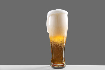 Glass of lager beer with thick froth on grey background