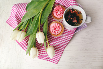 Still life with fresh bouquet of tulips, cupcakes and cup of tea on wooden table, top view
