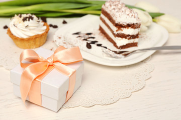 Fototapeta na wymiar Sweet creamy cake with flowers and present box on wooden table closeup